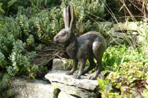 Bronze hare sculpture displayed outdoors in a garden setting among plants and stone